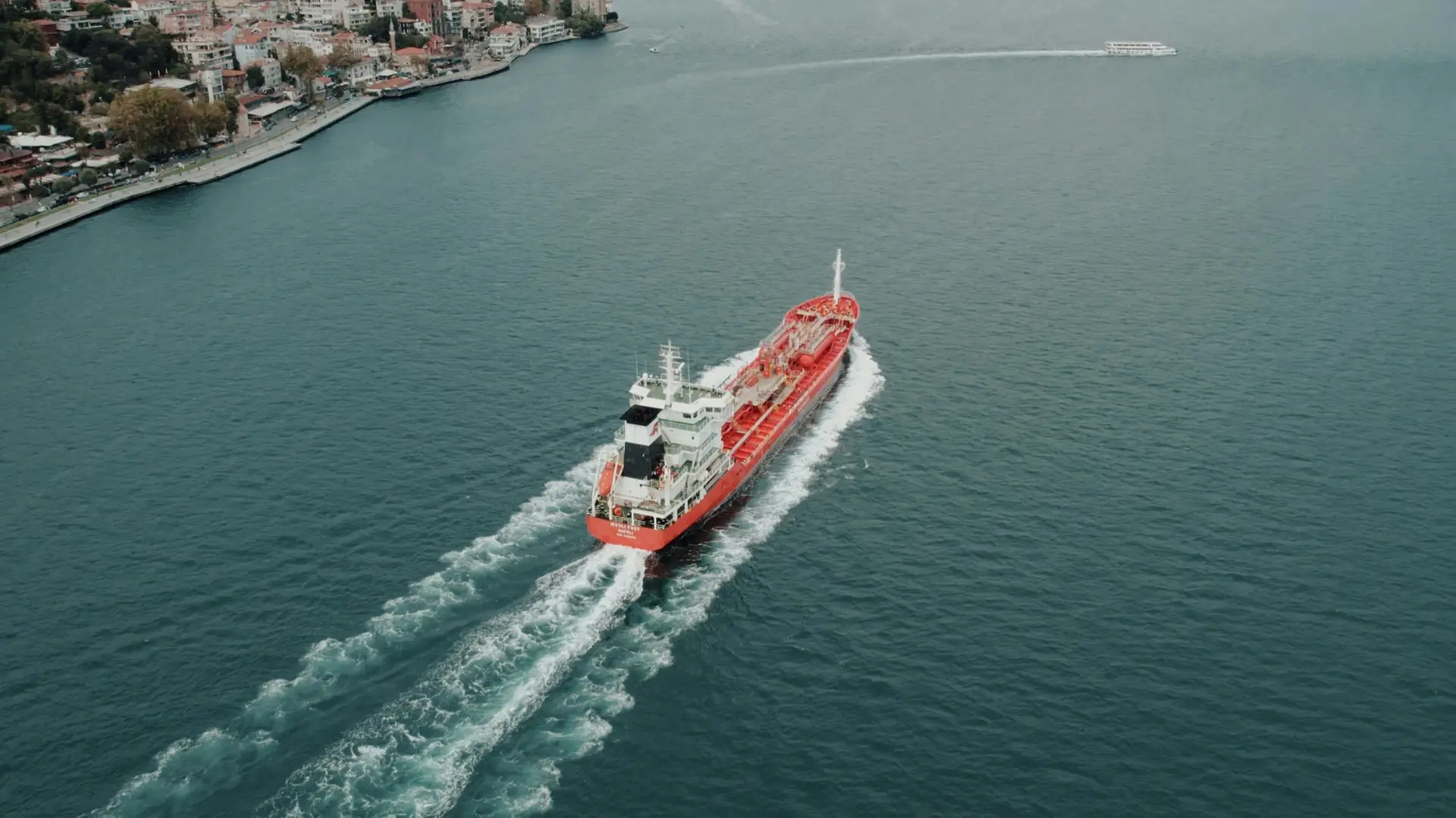 A red chemical tanker under way through a coastal strait, seen from above